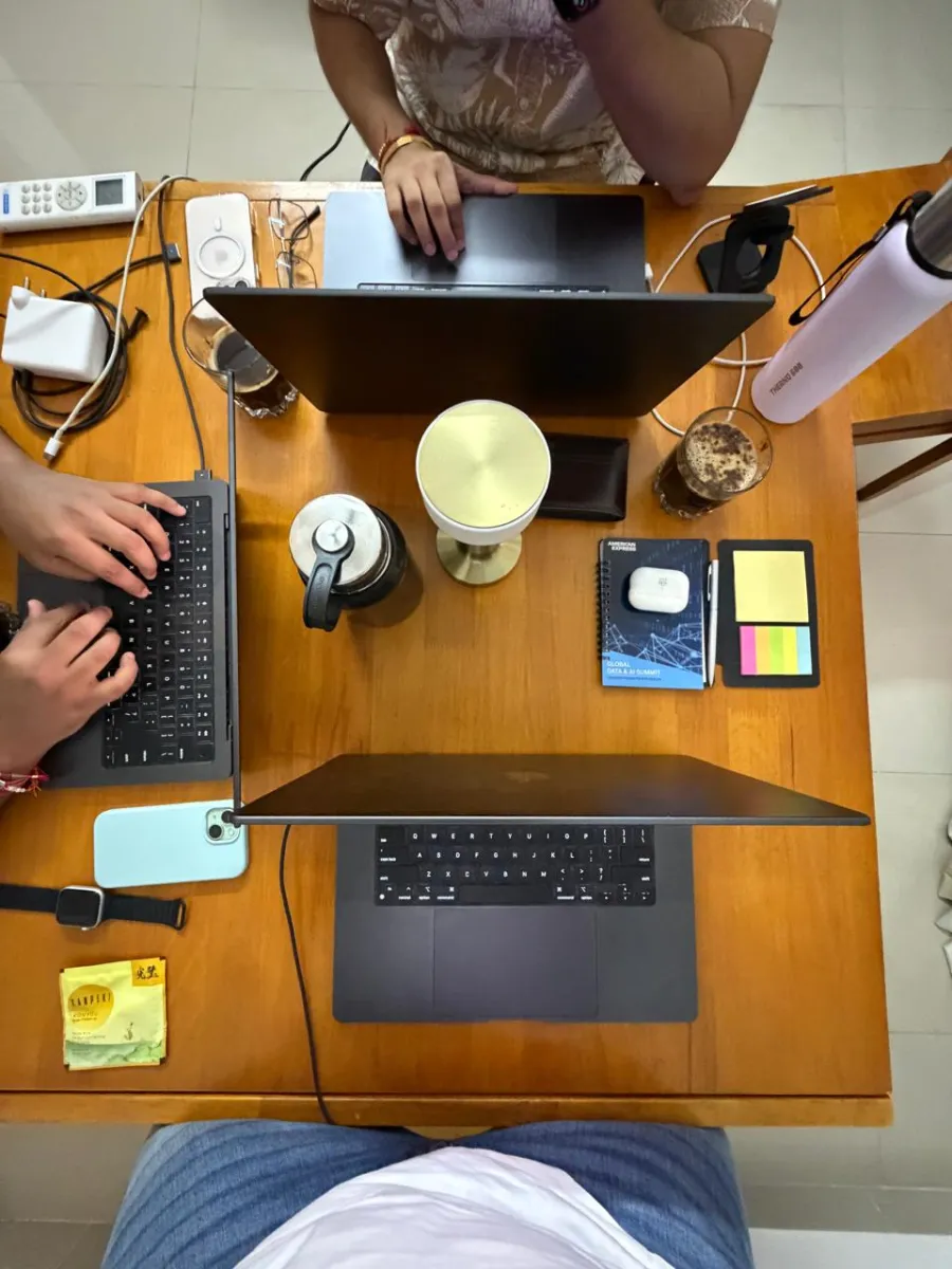 Three laptops, cold coffees and notebooks on a wooden dining table, seen from above